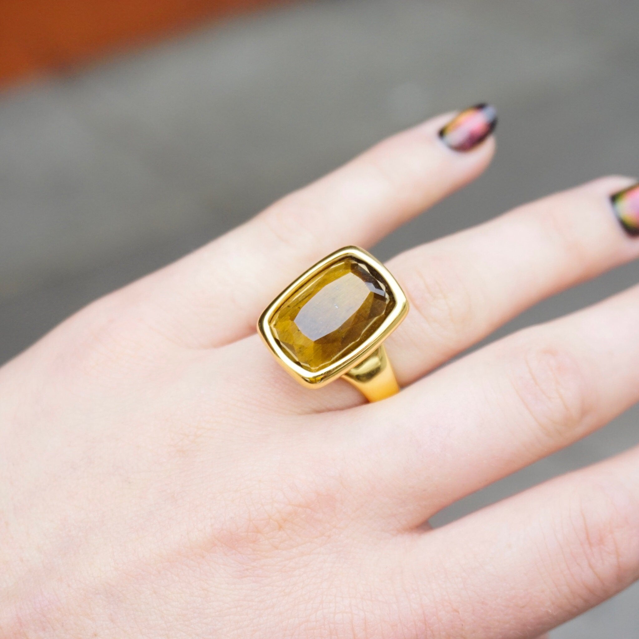14K gold tigers eye ring on a woman's hand, featuring a large rectangle cut tigers eye stone set in a gold mounting, made by Milor Italy using 14K gold over resin technique, shown against a gray background.