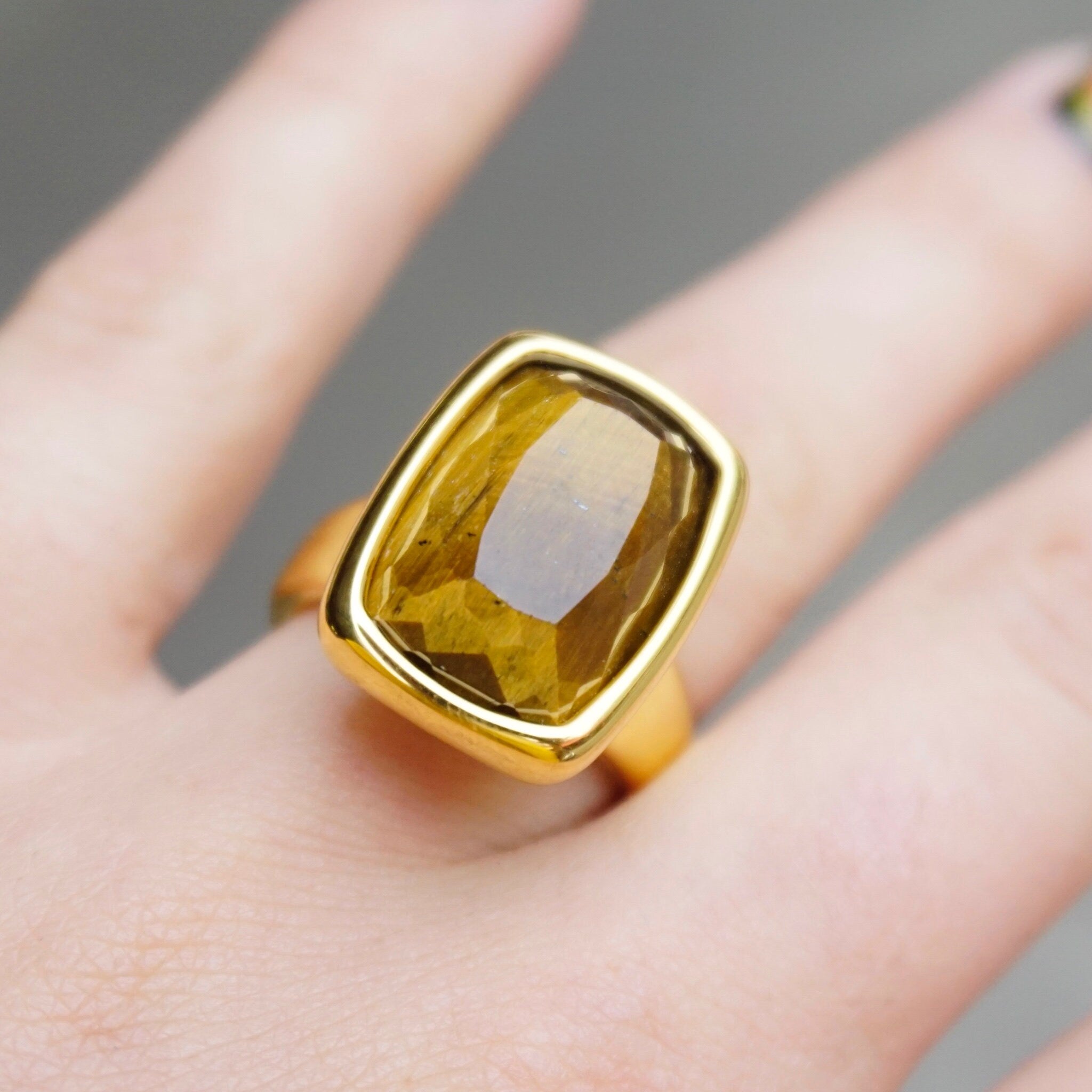 14K gold vintage ring featuring a large, rectangular-cut tiger's eye stone set in a chunky gold setting, shown on a person's hand against a gray background.
