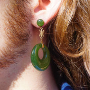 Closeup of a woman's ear wearing vintage 14K gold dangle earrings with green jade hoops and a Chinese symbol charm.