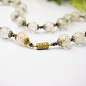Vintage Italian Murano glass bead choker necklace with clear and white wedding cake beads strung on gold tone metal links, photographed on white background.