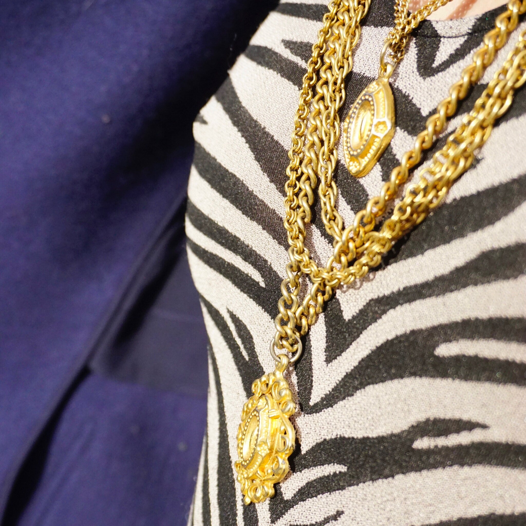 Vintage gold tone layered chain necklace with six strands and two ornate gold pendants against zebra print fabric