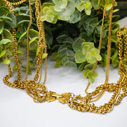Vintage gold tone layered chain necklace with 6 strands and 2 pendants displayed on greenery