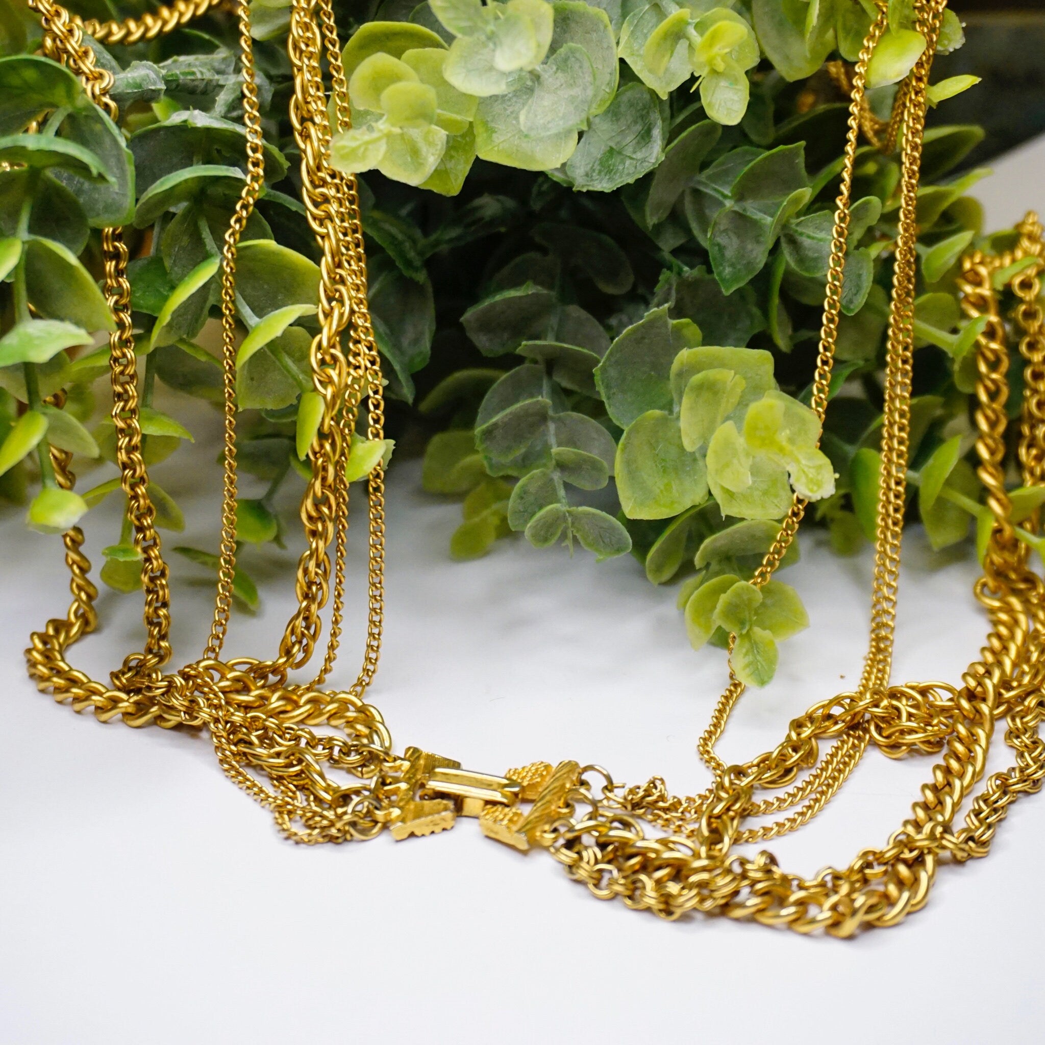 Vintage gold tone layered chain necklace with 6 strands and 2 pendants displayed on greenery