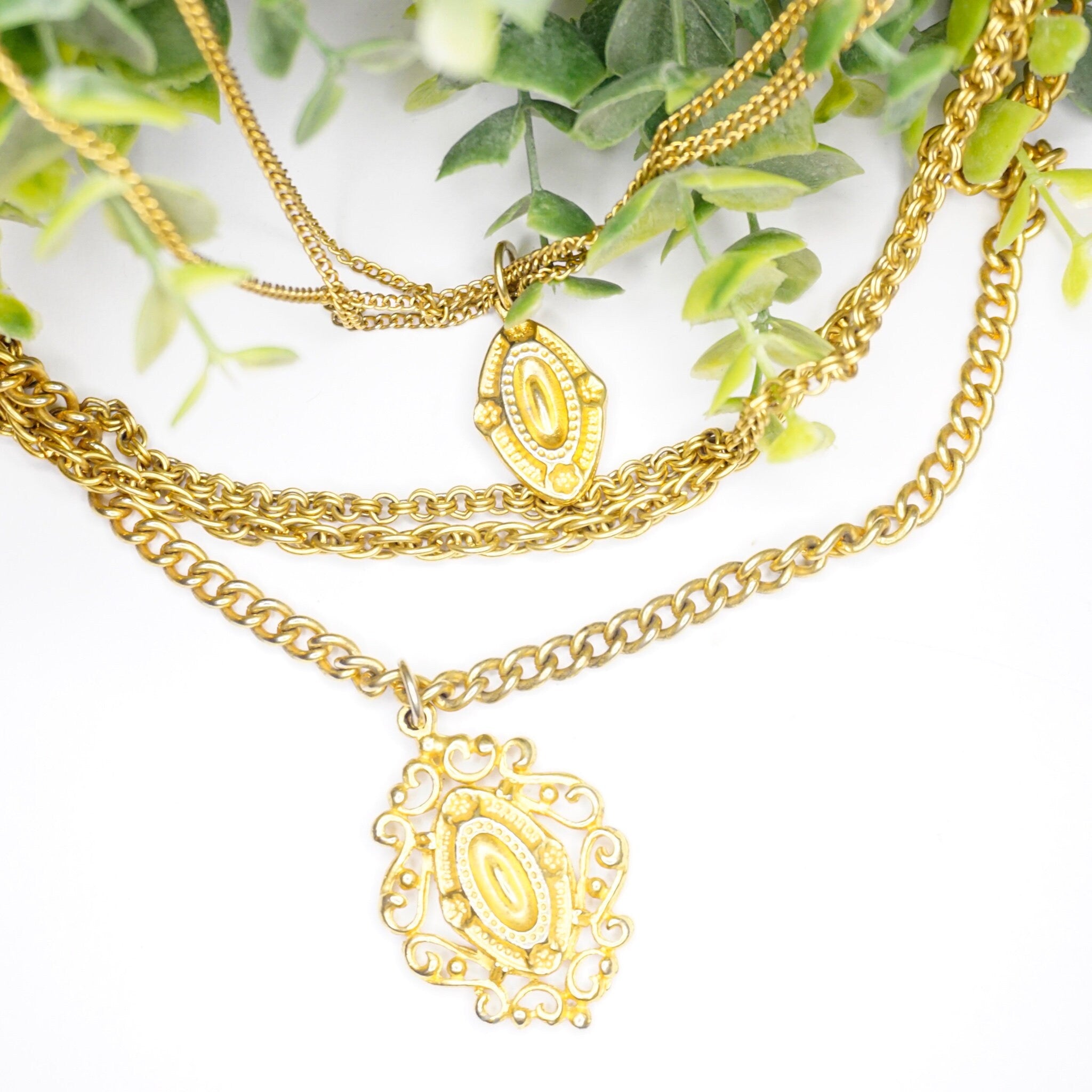 Vintage gold tone layered chain necklace with 6 strands and 2 ornate medallion pendants, displayed on greenery