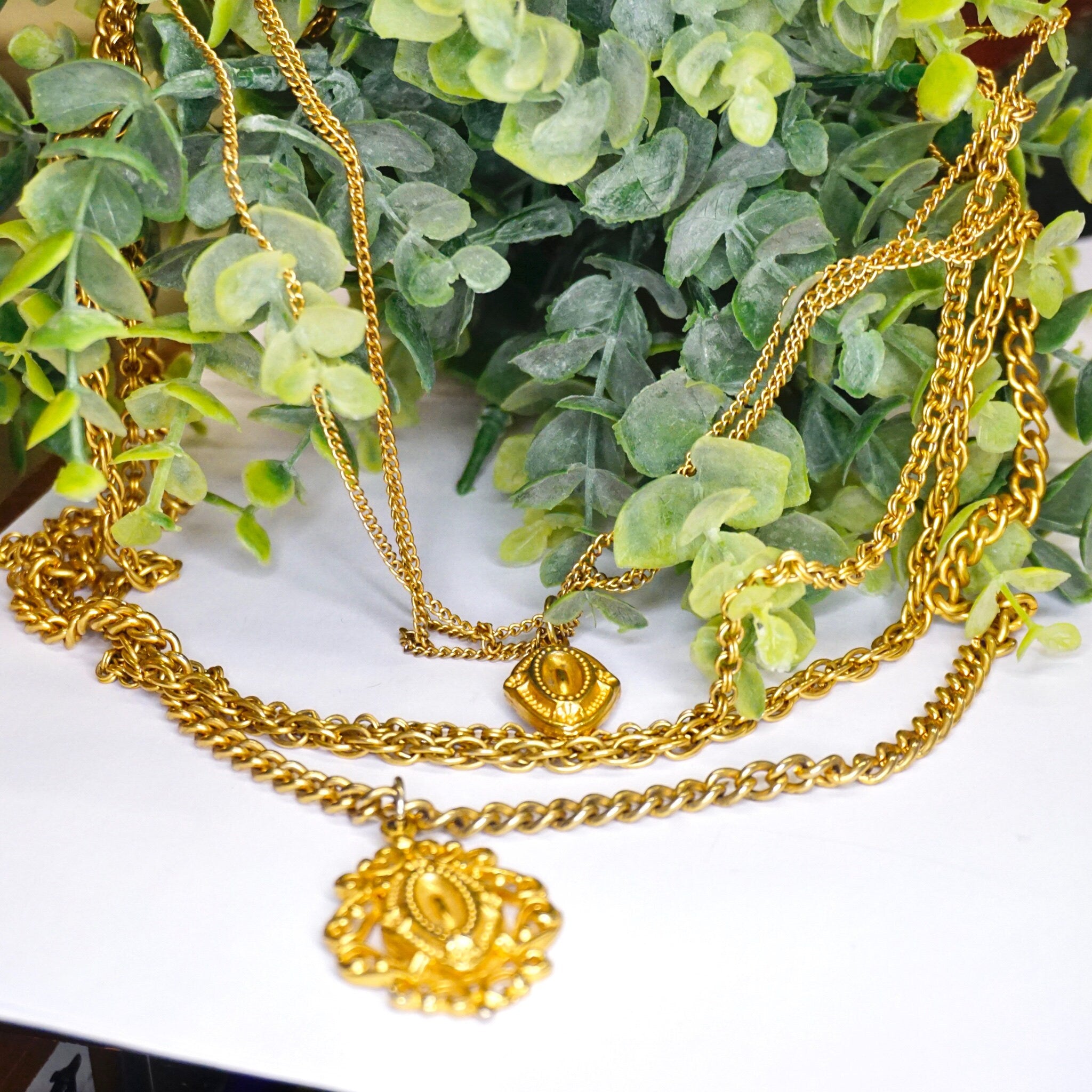 Vintage gold tone multi-strand chain necklace with pendants on greenery background