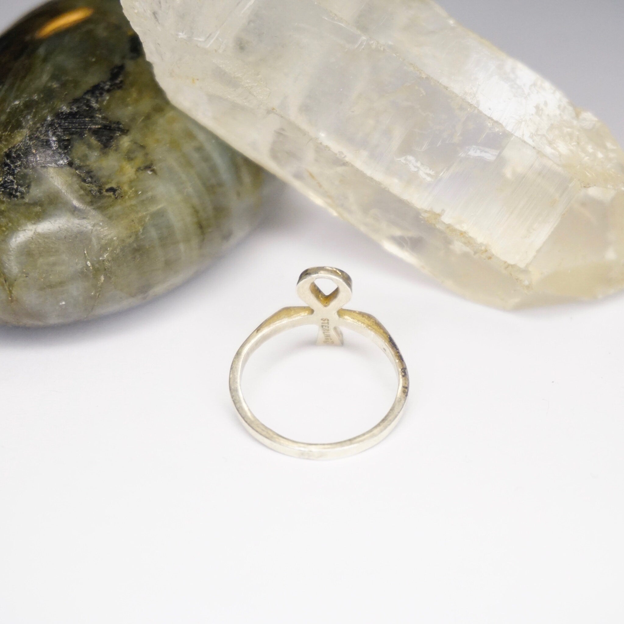 Vintage sterling silver ankh ring with Egyptian hieroglyphic symbol on a white background next to a green quartz crystal point