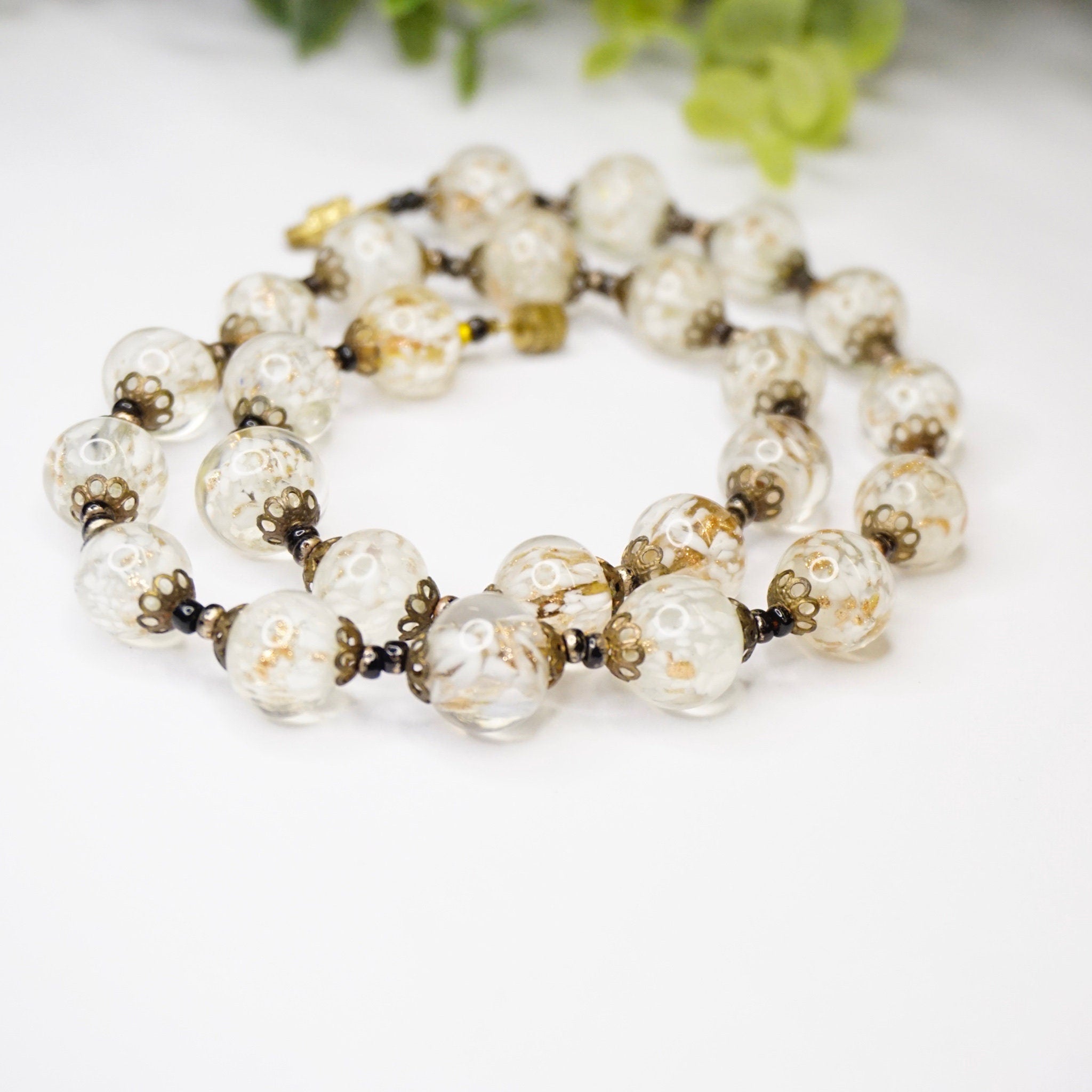 Vintage Italian Venetian Murano wedding cake glass bead choker necklace in clear and white colors, displayed with green foliage in the background.