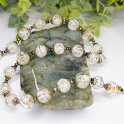 Vintage Italian glass bead choker necklace with white and clear Venetian Murano wedding cake beads on a decorative green stone slab surrounded by foliage.