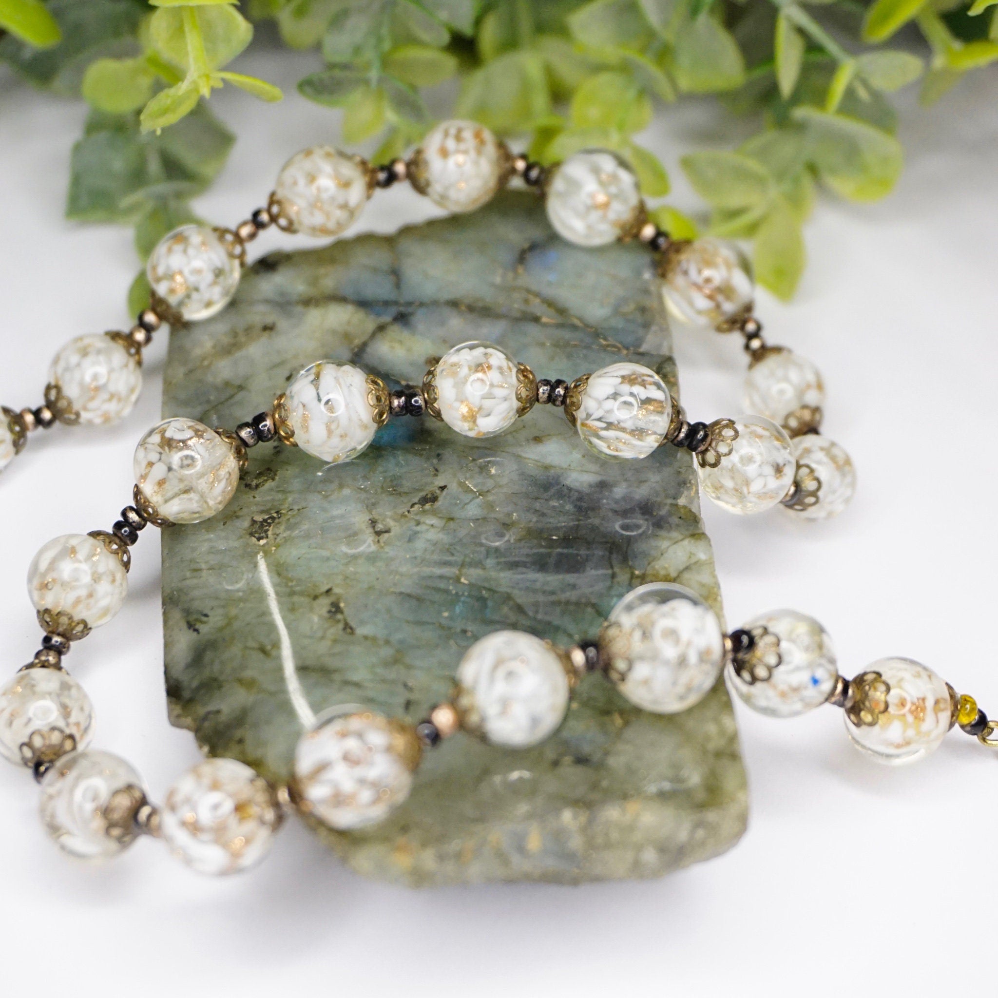 Vintage Italian glass bead choker necklace with white and clear Venetian Murano wedding cake beads on a decorative green stone slab surrounded by foliage.