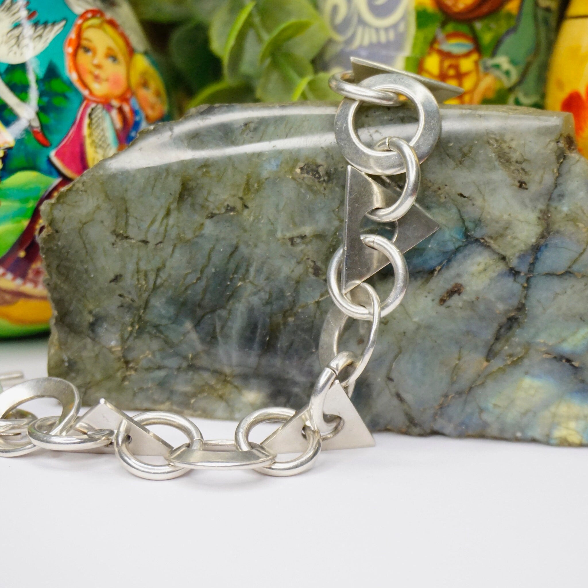 Vintage Taxco sterling silver link bracelet with modern geometric shapes on marbled stone background with colorful Russian nesting dolls in background.