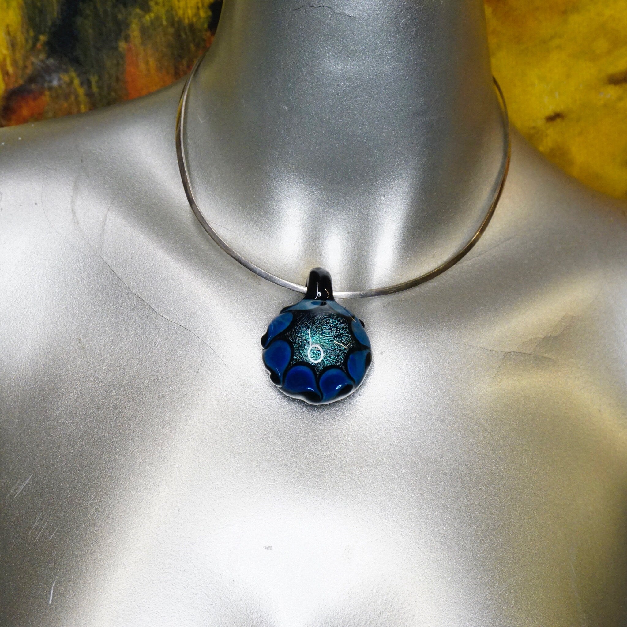 Blue and black abstract glass pendant with intricate fractal patterns, displayed on a mannequin bust against a colorful background.