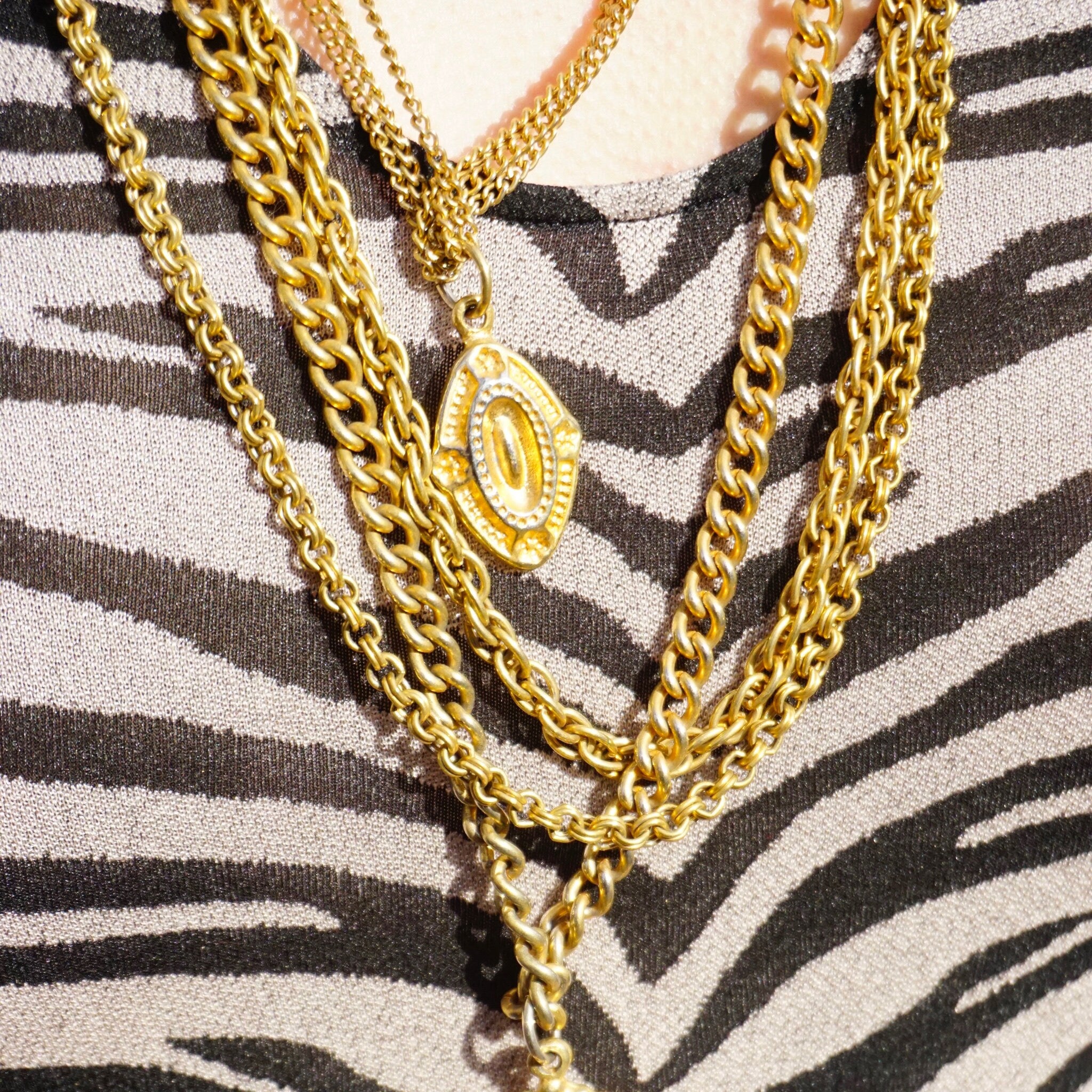 Vintage gold-tone layered chain necklace with multiple strands and pendant charms, displayed on zebra print fabric
