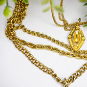 Vintage gold tone layered chain necklace featuring multiple strands and ornate gold pendants, set against a white background with green foliage accents.