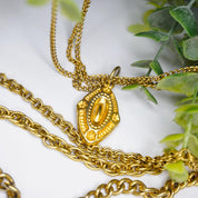 Vintage gold tone layered chain necklace with multiple strands and ornate pendants, displayed on white background with green foliage accents.