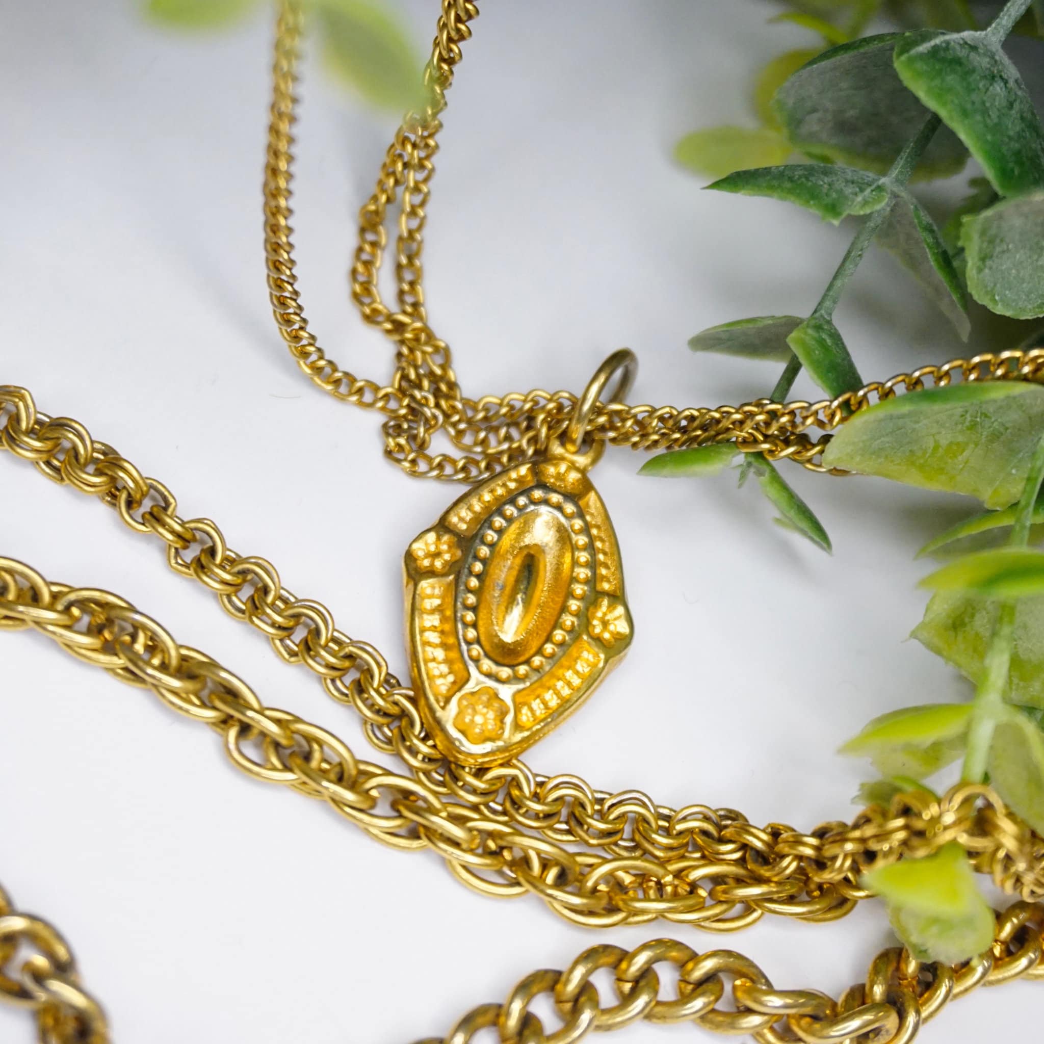 Vintage gold tone layered chain necklace with multiple strands and ornate pendants, displayed on white background with green foliage accents.