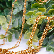 Vintage gold tone layered chain necklace with multiple strands and pendants resting on green leaves