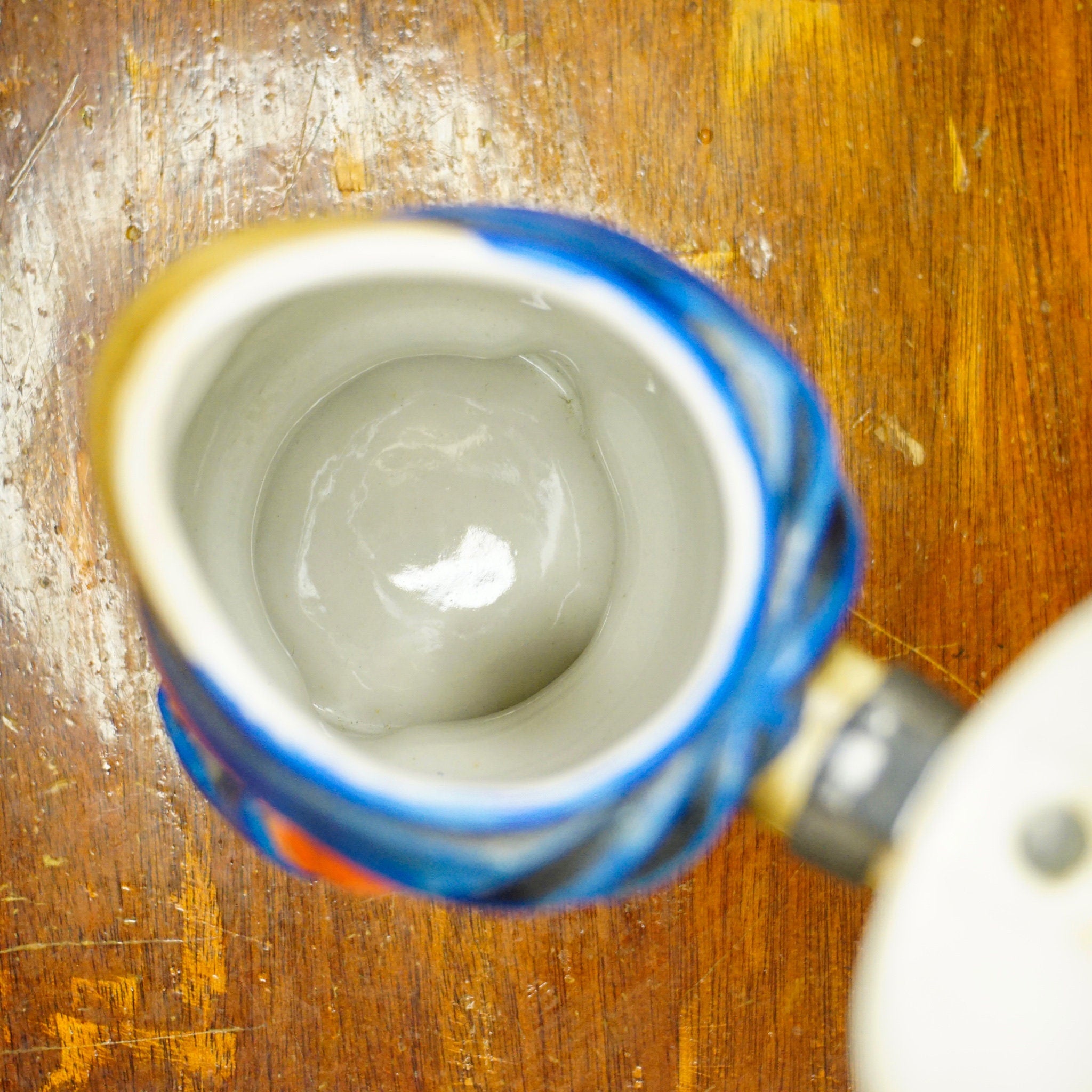 Vintage 1975 Original Anheuser Busch Bud Man beer stein, made by Ceramarte in Brazil, showing the inside bottom of a blue and white ceramic beer stein on a wooden surface