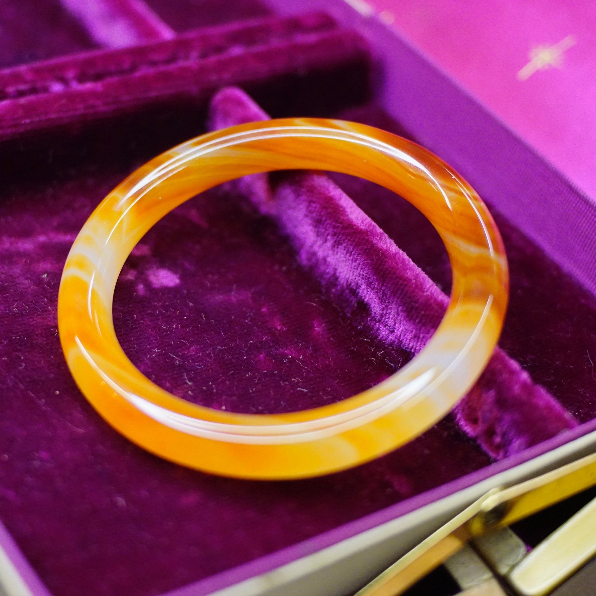 Vintage 1960s Murano glass bangle in marbled orange tones with semi-translucent swirl design, resting on purple velvet jewelry box