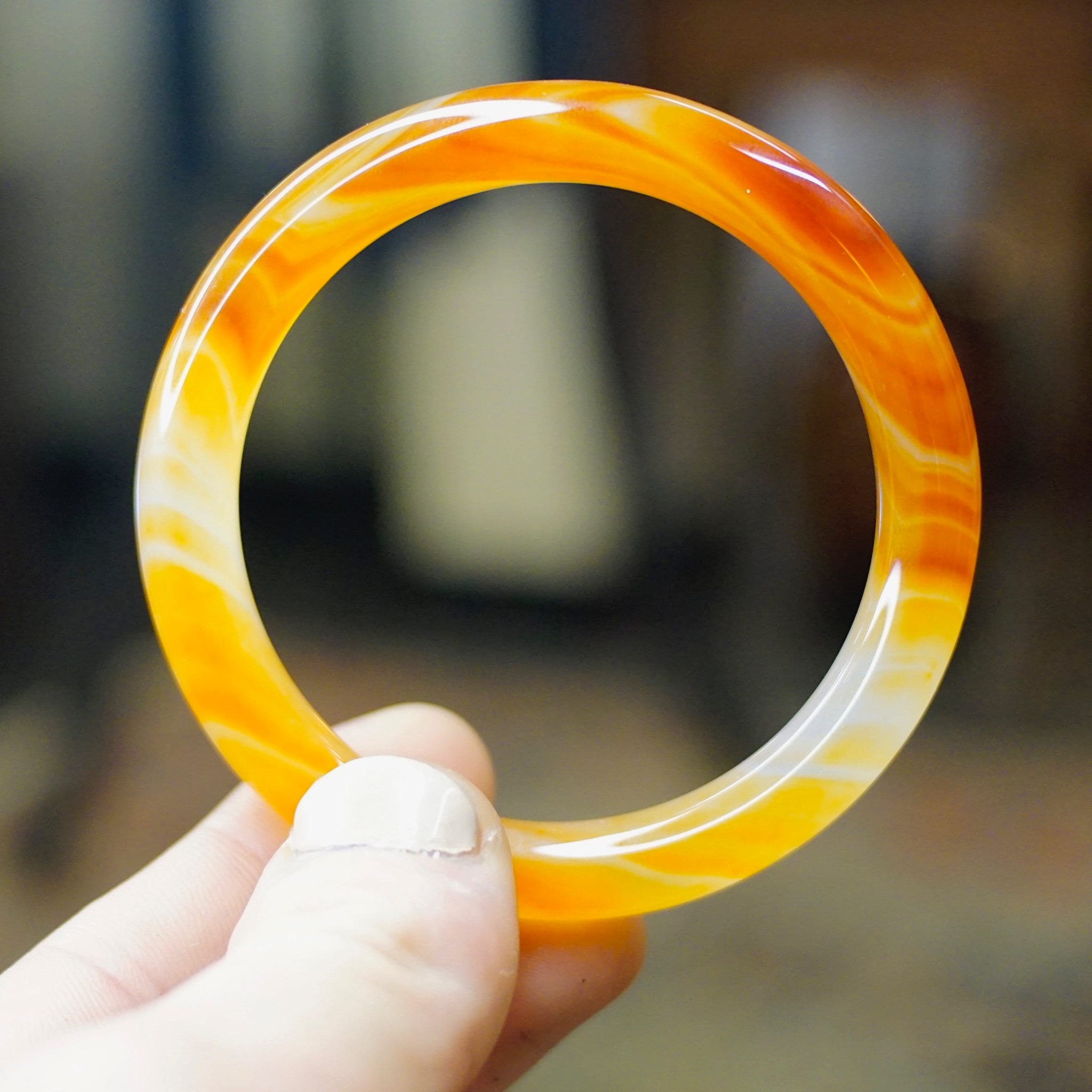 Hand holding a semi-translucent orange glass bangle with swirl design, likely vintage Venetian or Murano glass from the 1960s, in front of a blurred background.