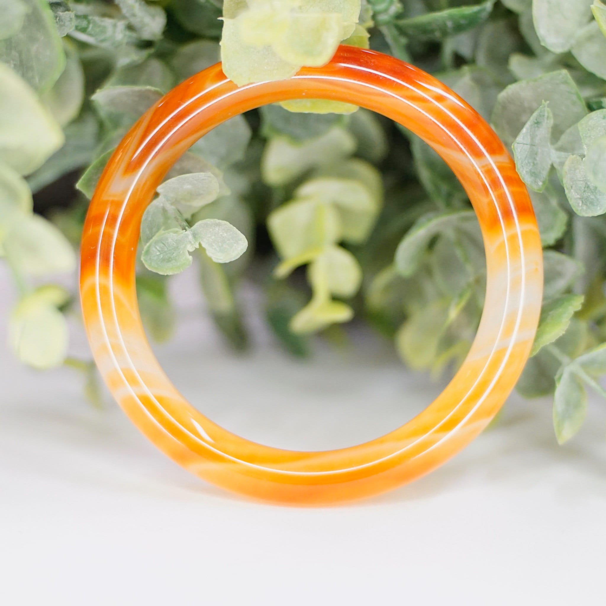 Vintage orange Murano glass bangle bracelet with marbled swirl design from the 1960s, shown with greenery in background