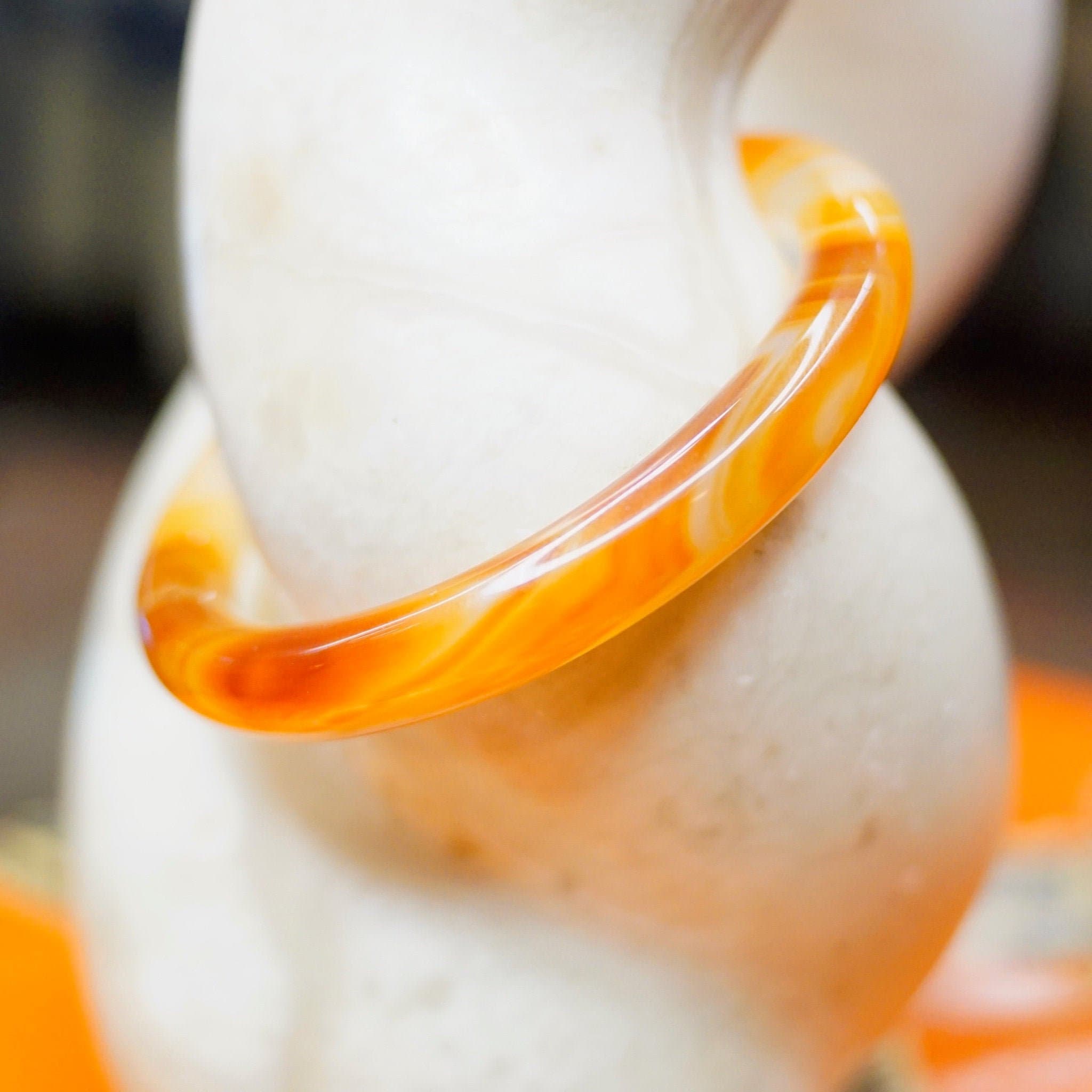 Vintage 1960's Murano glass bangle bracelet with marbled orange and white semi-translucent swirl design, displayed on a white surface with orange accents in the background.