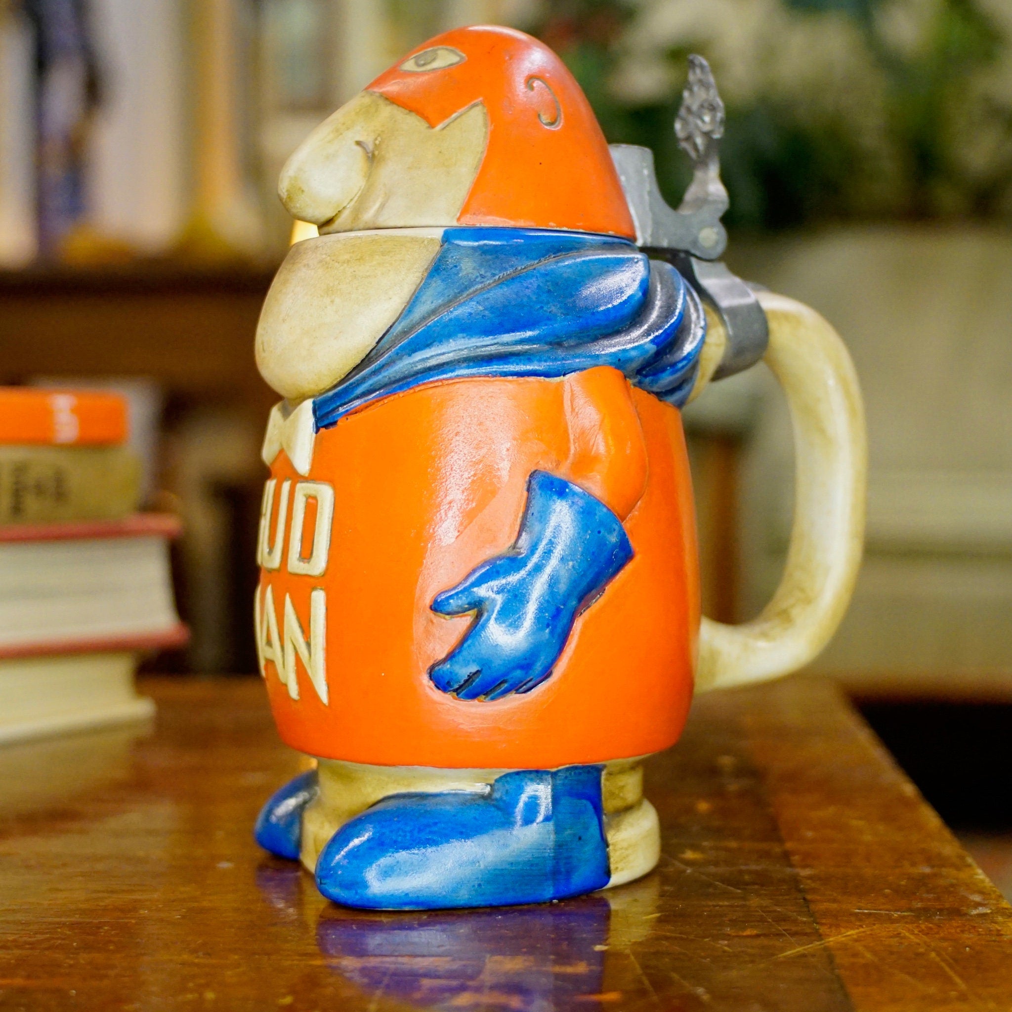 Vintage 1975 Anheuser Busch Bud Man ceramic beer stein featuring the debut Bud Man mascot figurine in orange and blue, made by Ceramarte in Brazil. Collectible Budweiser advertising character stein with "Bud Man 75" text on the back.
