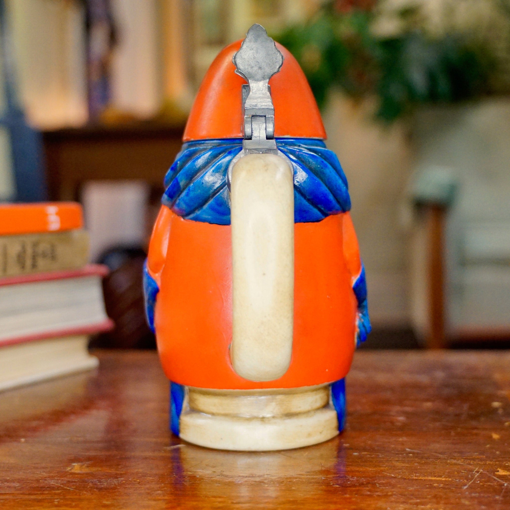 Vintage 1975 Anheuser Busch Bud Man ceramic beer stein figurine in orange and blue, featuring a rotund body and pointed cap, made by Ceramarte in Brazil. Collectible Bud Man debut stein displayed on a wooden surface.
