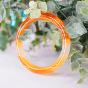 Vintage 1960's Murano glass bangle bracelet featuring a marbled orange swirl design on semi-translucent glass, showcased on greenery background