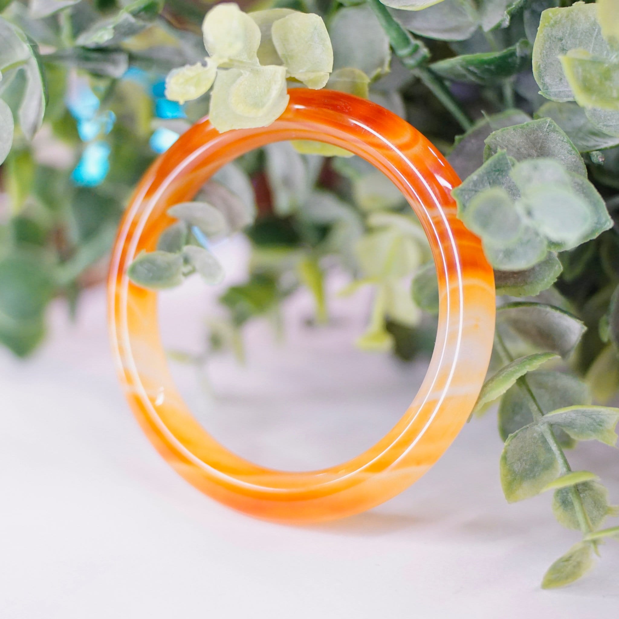 Vintage 1960's Murano glass bangle bracelet featuring a marbled orange swirl design on semi-translucent glass, showcased on greenery background