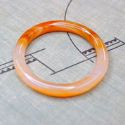 Vintage 1960's Murano glass bangle featuring marbled orange and white semi-translucent swirl design on neutral fabric background