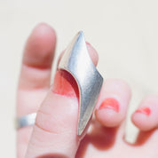 A hand wearing a vintage sterling silver lightning bolt ring with elongated points on the finger, against a light background.