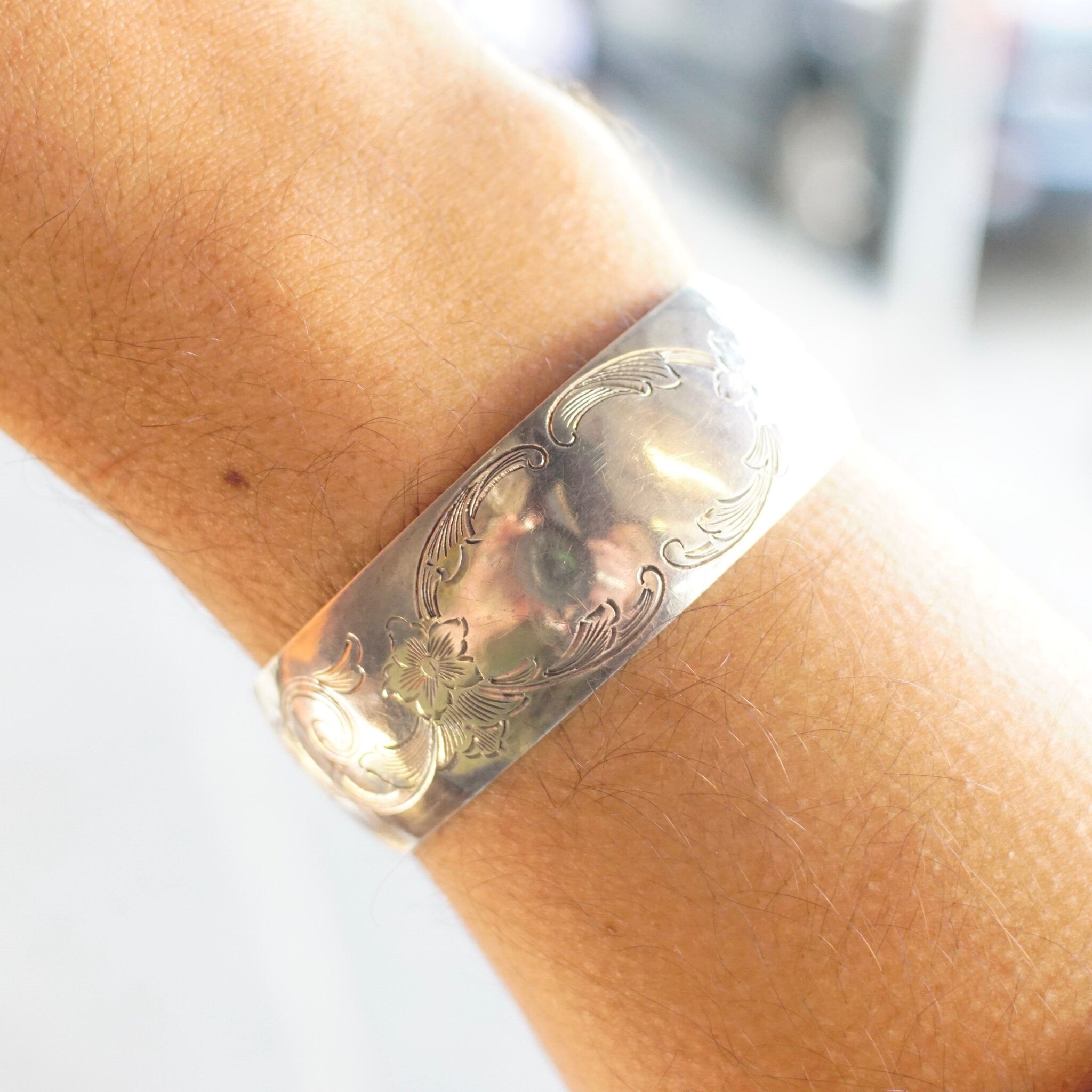Vintage sterling silver cuff bracelet with etched floral design on wrist, close-up view showing intricate engraved details on the silver cuff with space for monogram initials.