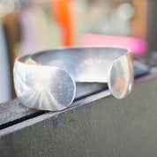 Vintage sterling silver cuff bracelet with etched floral design on wooden surface
