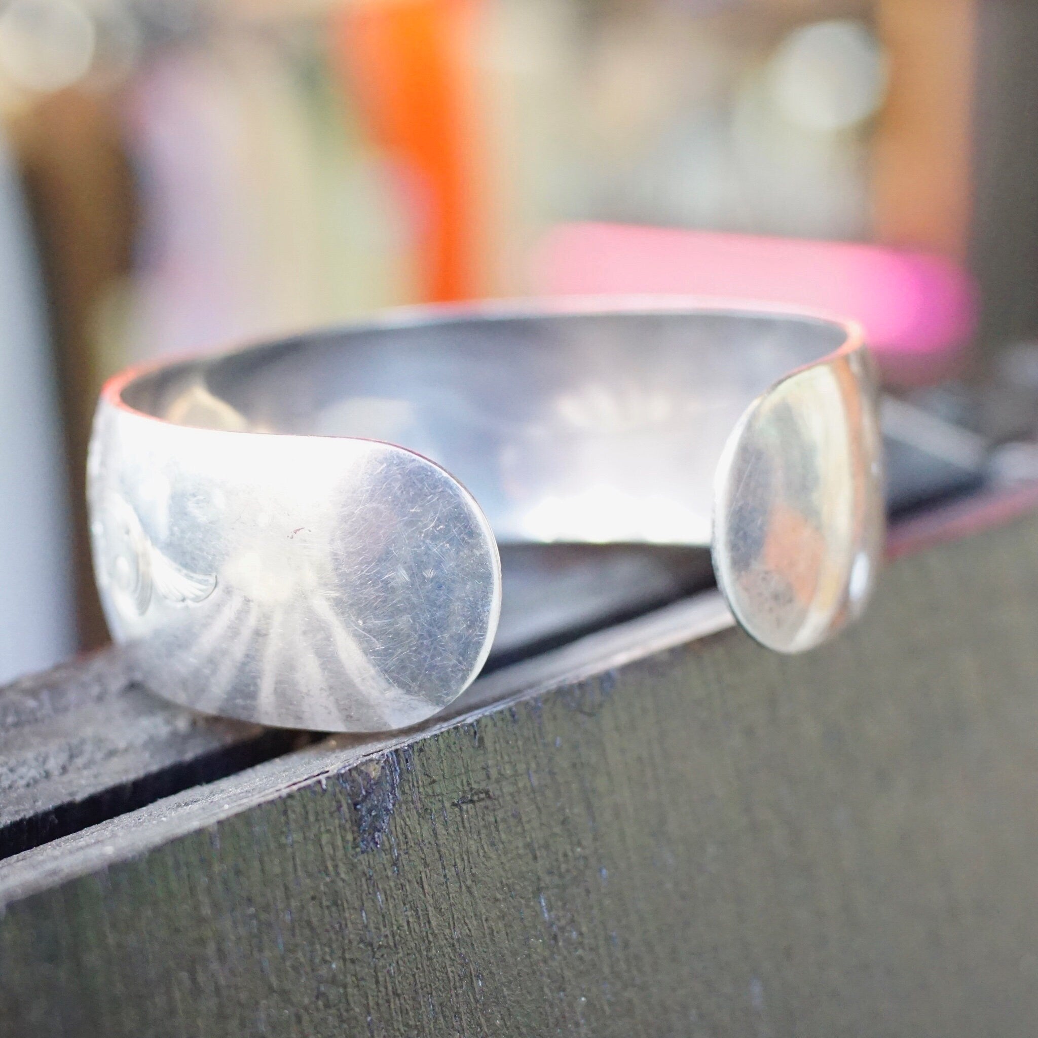 Vintage sterling silver cuff bracelet with etched floral design on wooden surface