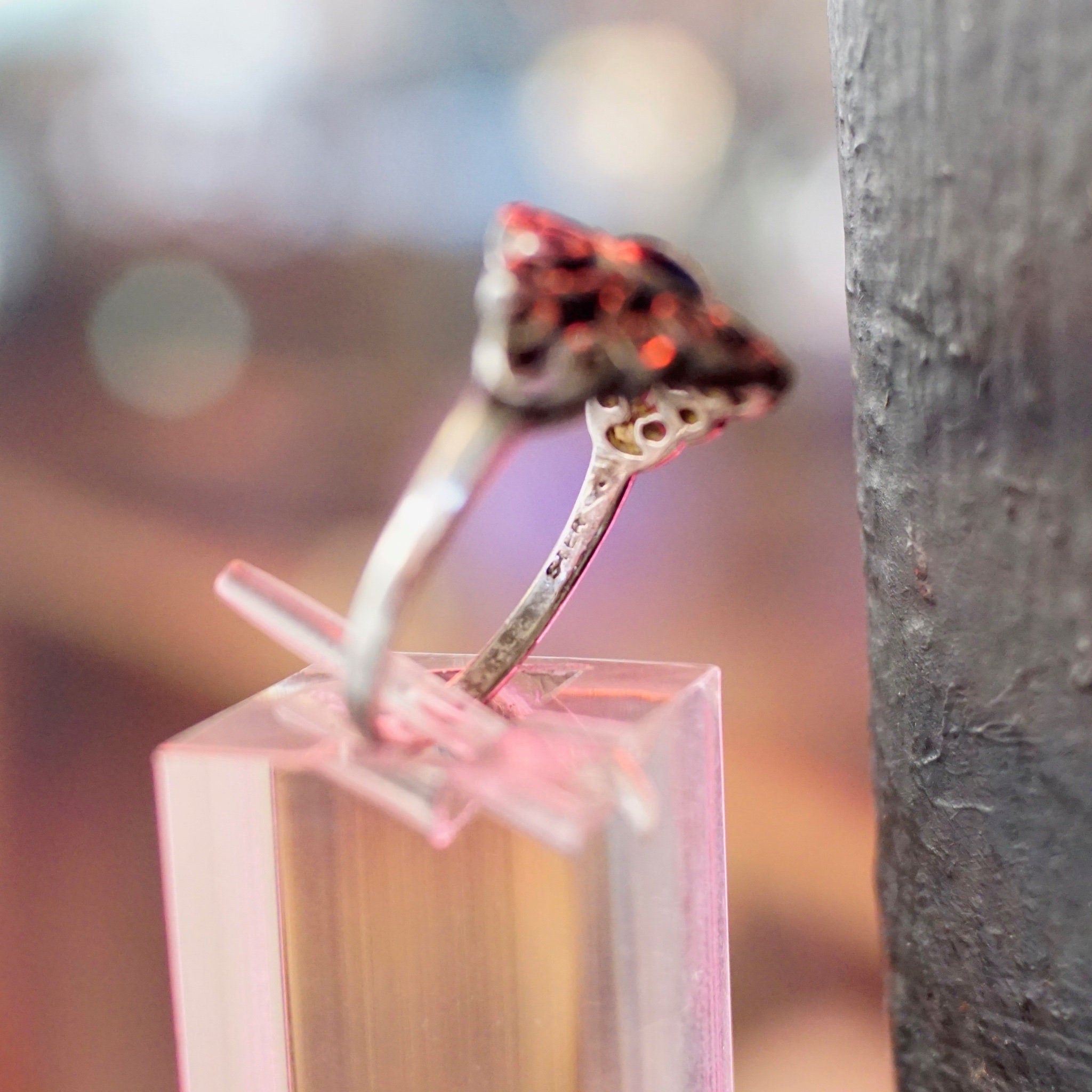 Two orange and black spotted butterfly wings attached to a sterling silver ring standing upright on a wooden surface, with blurred bokeh background.