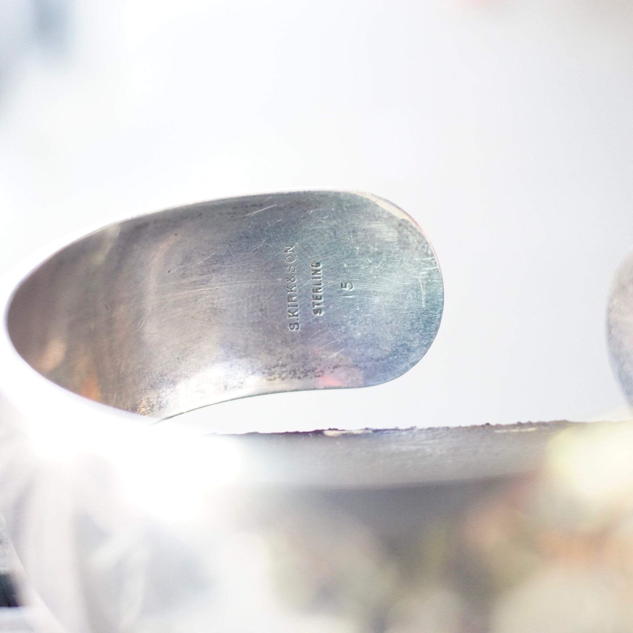 Vintage S. Kirk & Son sterling silver cuff bracelet with etched floral design and space for engraved monogram, shown from the side view on a white surface with glitter.