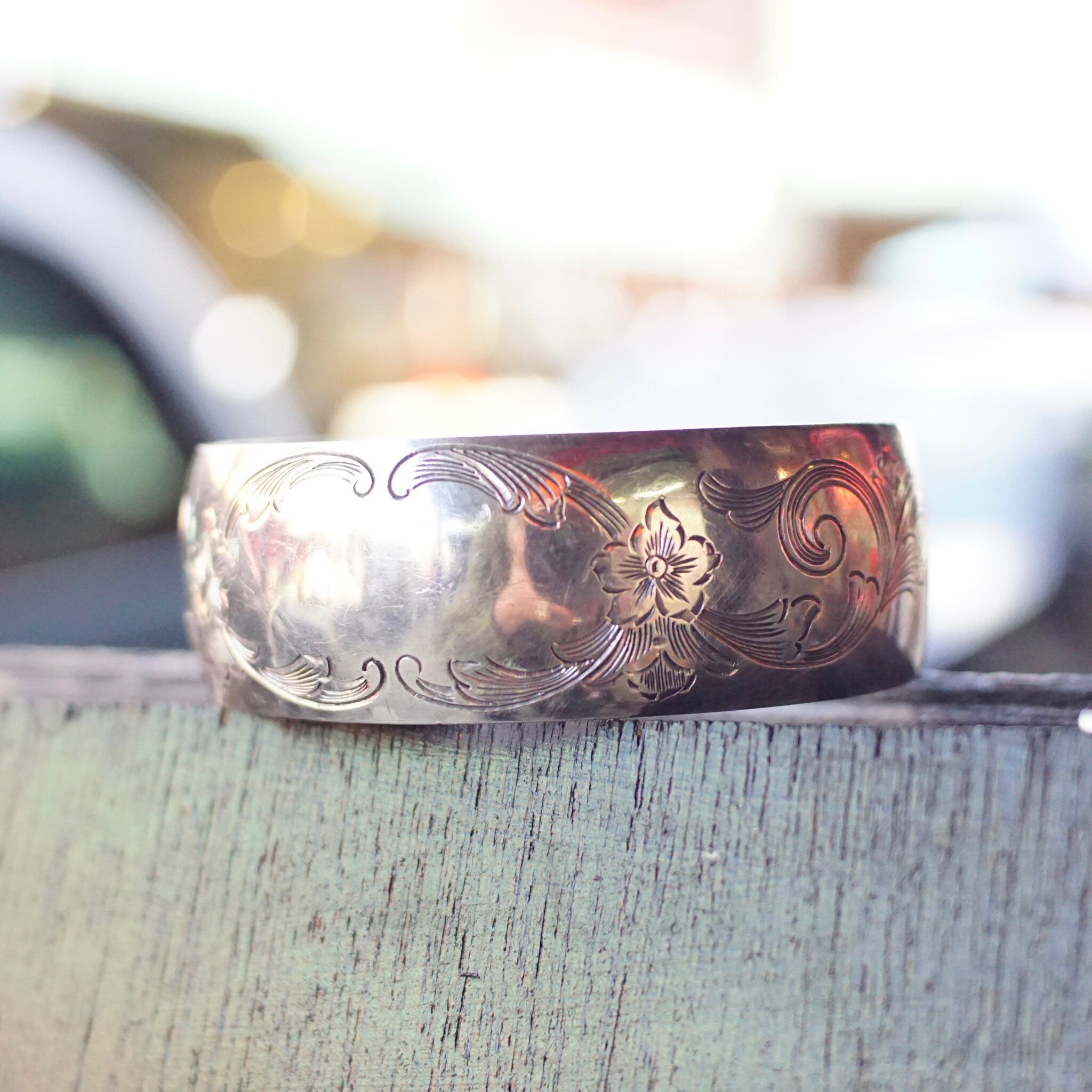 Vintage sterling silver cuff bracelet with intricate etched floral design, made by S. Kirk & Son. The ornate silver cuff features a smooth oval space in the center, perfect for engraving a monogram or initials. The antique bracelet is shown resting on a weathered wooden surface.