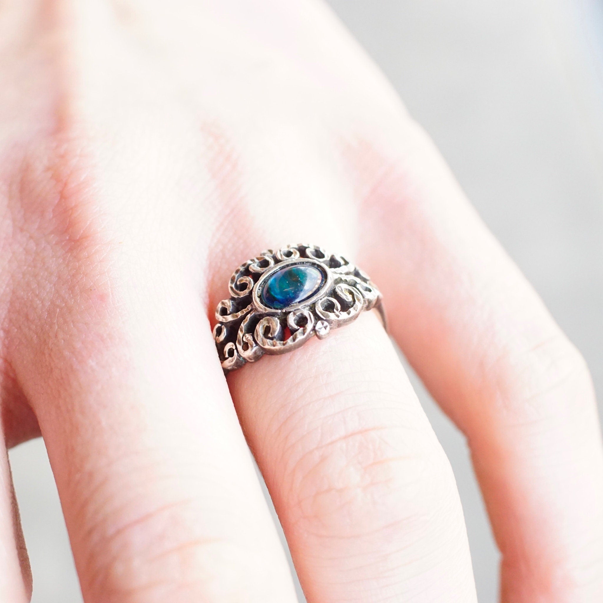 Vintage ornate sterling silver ring with iridescent blue glass stone on textured, hammered silver band, size 9 1/4 US, shown on person's finger.
