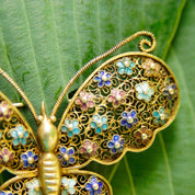 Antique Chinese silver filigree butterfly brooch with gold wash, featuring hand-carved nephrite jade, intricate enamel work, and a delicate wedding basket design, showcasing the artisan craftsmanship of devil's work metalwork technique.