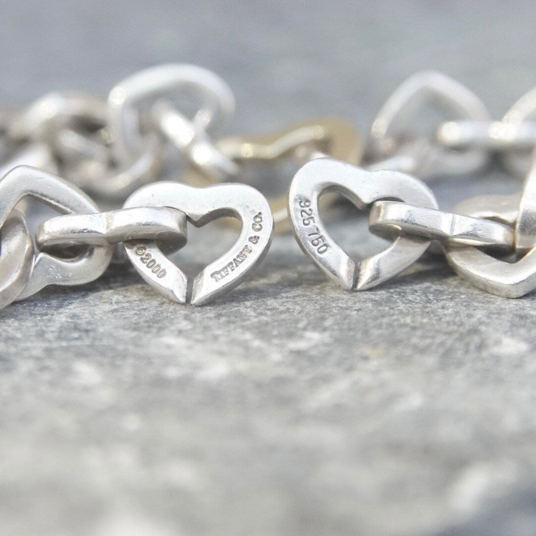 Vintage Tiffany & Co 18K gold and sterling silver heart link bracelet, curb chain design, measuring 7 1/2 inches long, close-up view on gray background