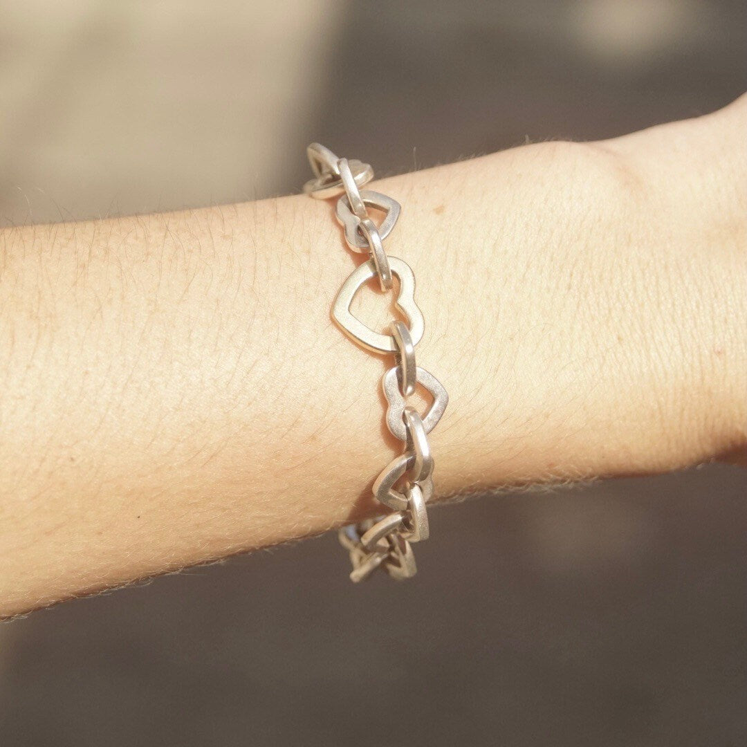 Tiffany & Co. two-tone heart link bracelet in 18K gold and sterling silver on wrist, close-up view of vintage curb chain jewelry piece with alternating gold and silver heart-shaped links, 7 1/2 inches long.