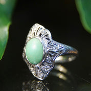 Vintage 18K white gold art deco filigree ring with matte green turquoise center stone and diamond encrusted shield design, size 7 3/4 US.