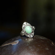 Vintage 18K white gold Art Deco filigree ring featuring a matte green turquoise stone surrounded by diamond encrusted accents in a shield design, sized 7 3/4 US, photographed on a dark rock surface.