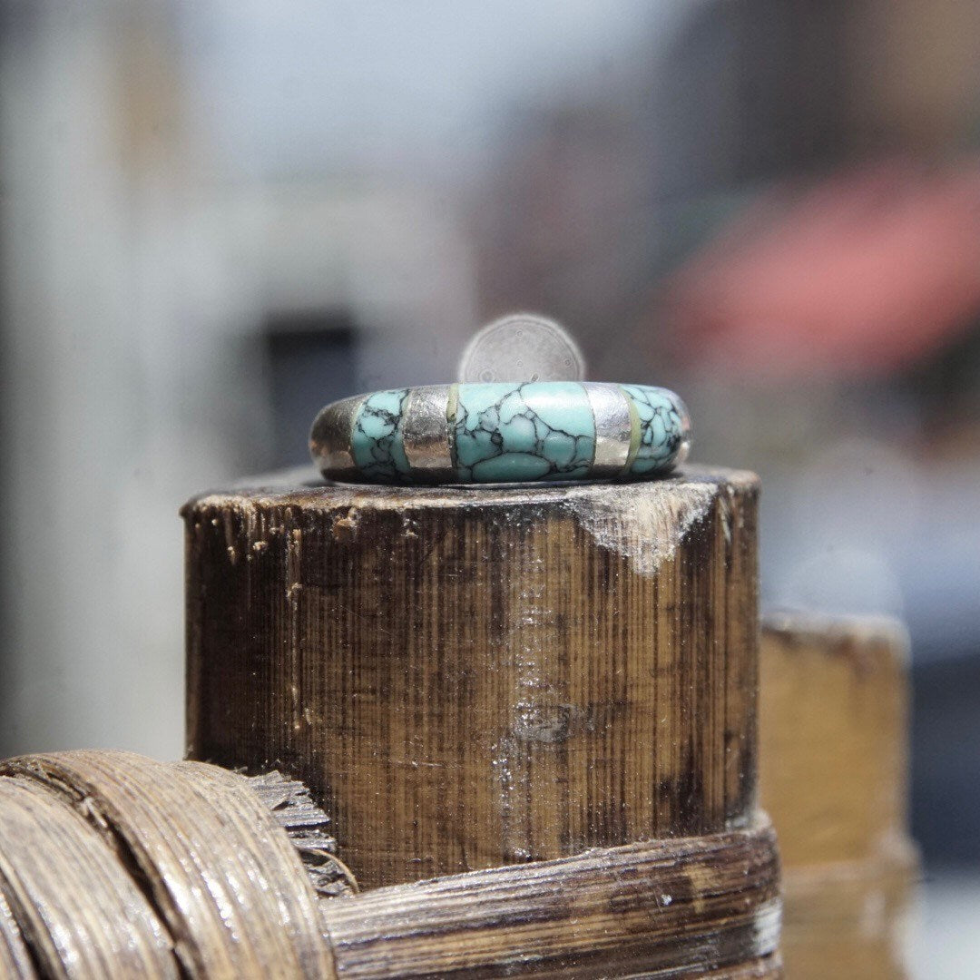 Vintage sterling silver tapered band ring with light blue speckled turquoise inlay, stacked on weathered wooden surface, selective focus