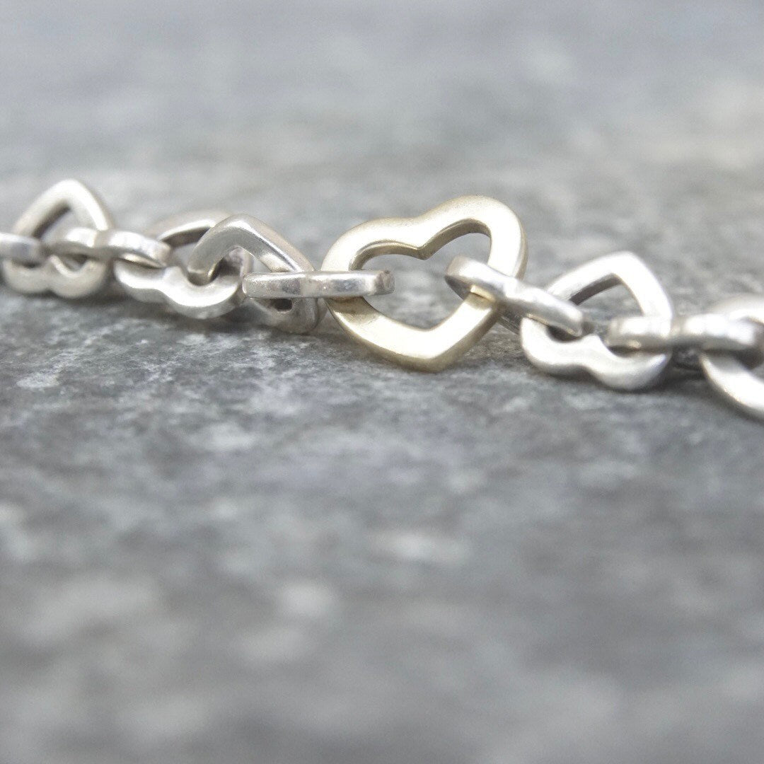 Vintage Tiffany & Co. sterling silver heart link bracelet with alternating 18K gold heart links, close-up view on gray background