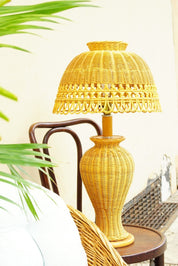 Vintage mid-century modern wicker table lamp with matching umbrella-shaped shade, in natural wicker finish, against tropical greenery background