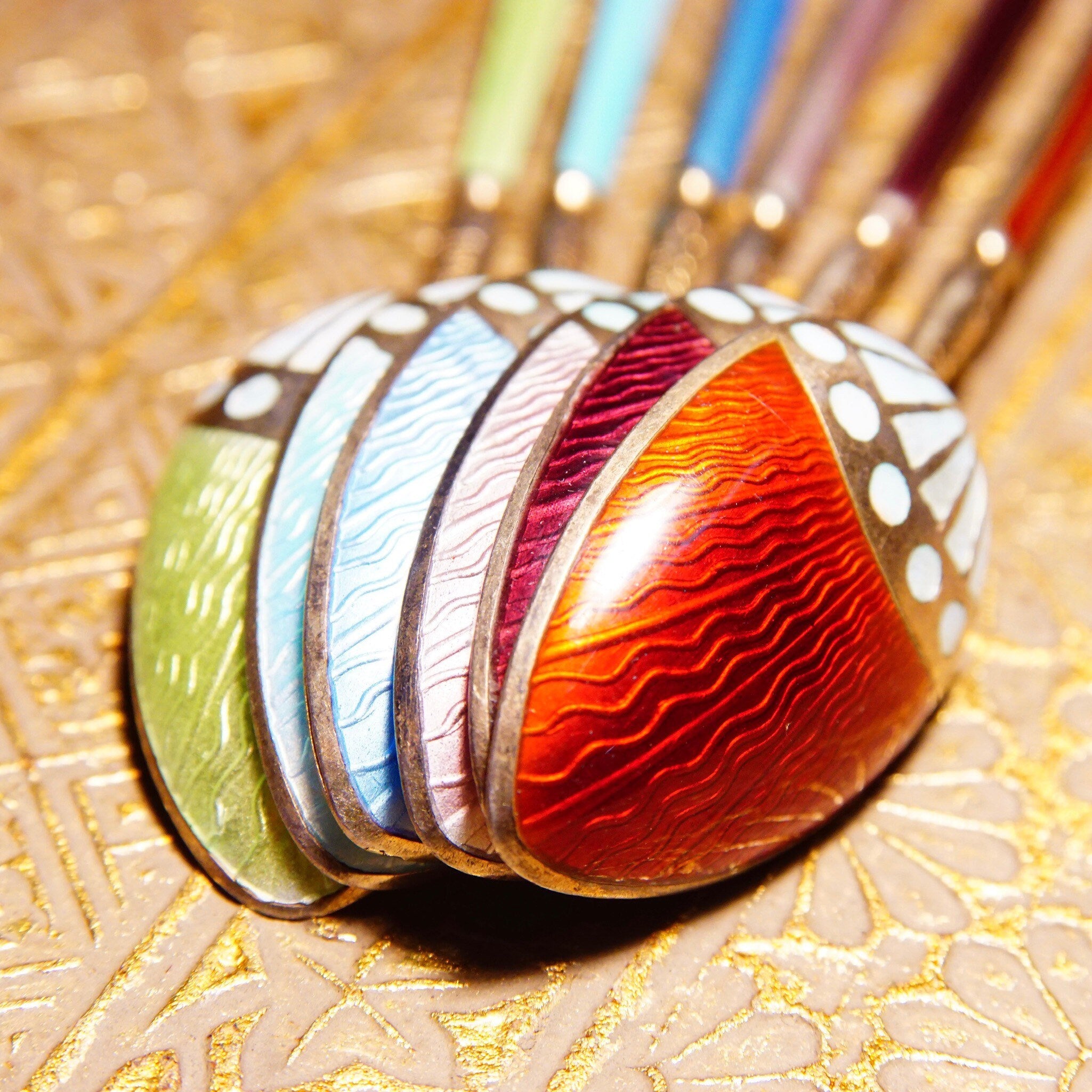 Antique Art Deco sterling silver guilloche enamel demitasse spoon set with colorful patterns resting on ornate gold fabric