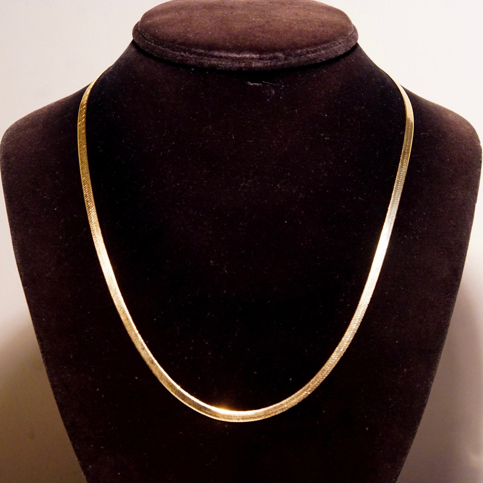 Vintage 14K yellow gold herringbone chain necklace displayed on black velvet bust, showing elegant minimalist design with 3mm flat herringbone links and 20 inch length, suitable as unisex jewelry piece.