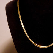Vintage 14K yellow gold herringbone chain necklace on black velvet display, showing flat 3mm chain links and delicate gold shimmer, unisex minimalist Italian gold jewelry, 20 inches long.