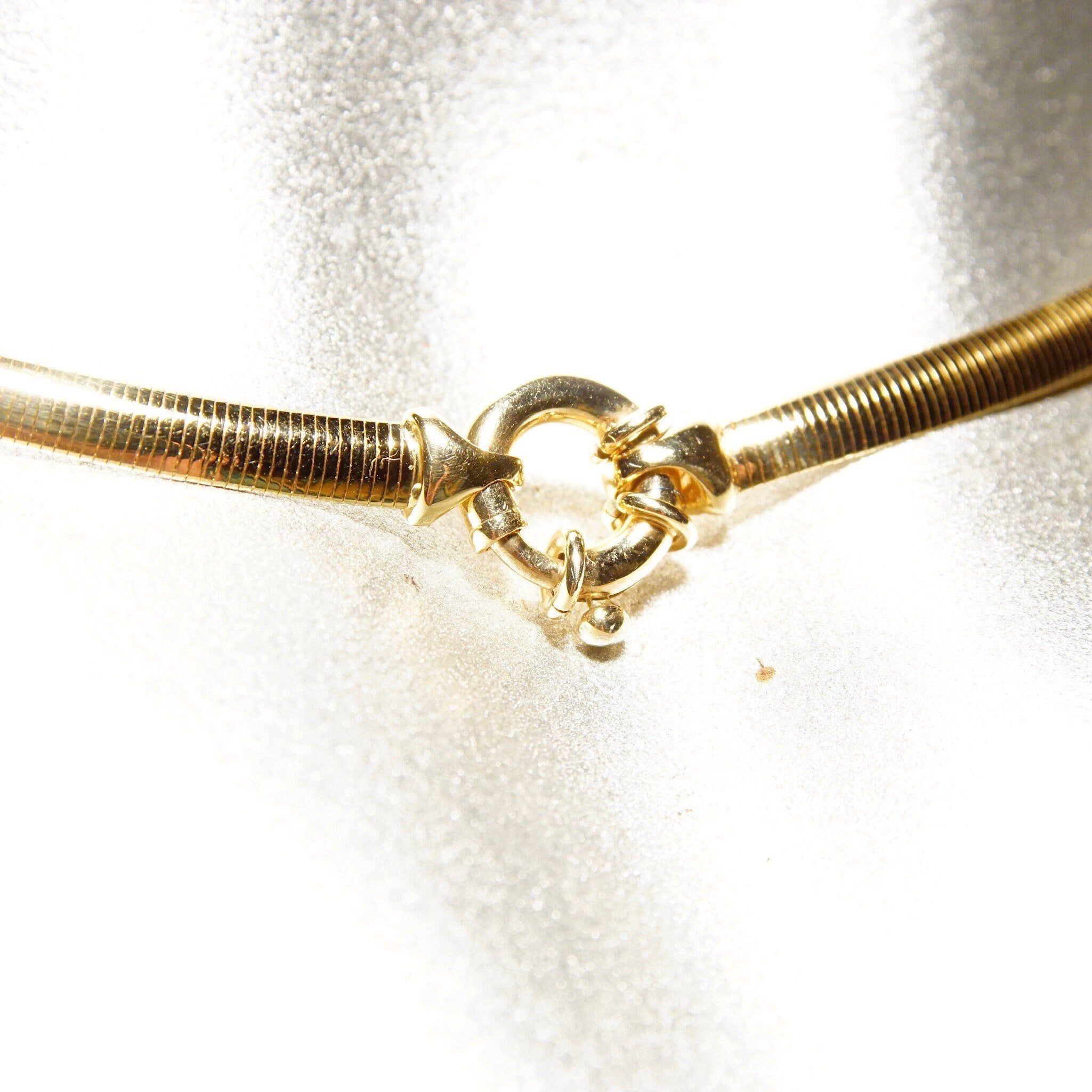 Vintage Italian 14K yellow gold omega collar necklace with minimalist design, 4mm thick, lustrous finish, made in Italy, 585 stamped, 16 inches long, closeup view on shimmery background.